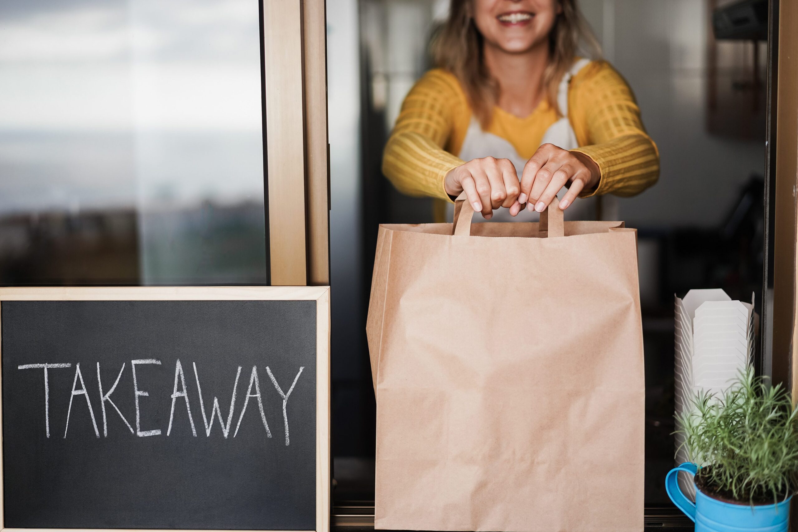 Ghost kitchen - Young woman preparing takeaway food for fast delivery inside ghost kitchen - Focus on hands holding bag