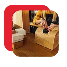 Staff member packaging a food order in a paper bag for pickup